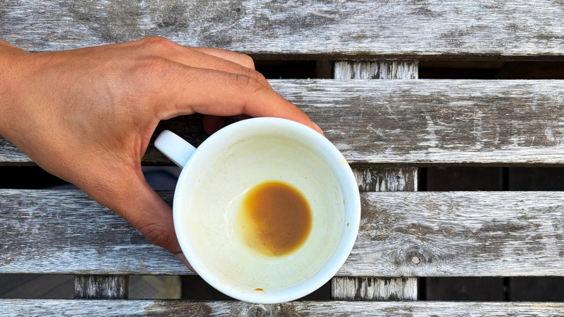 Eine Hand greift auf einem verwitterten Holztisch nach einer leeren Kaffeetasse